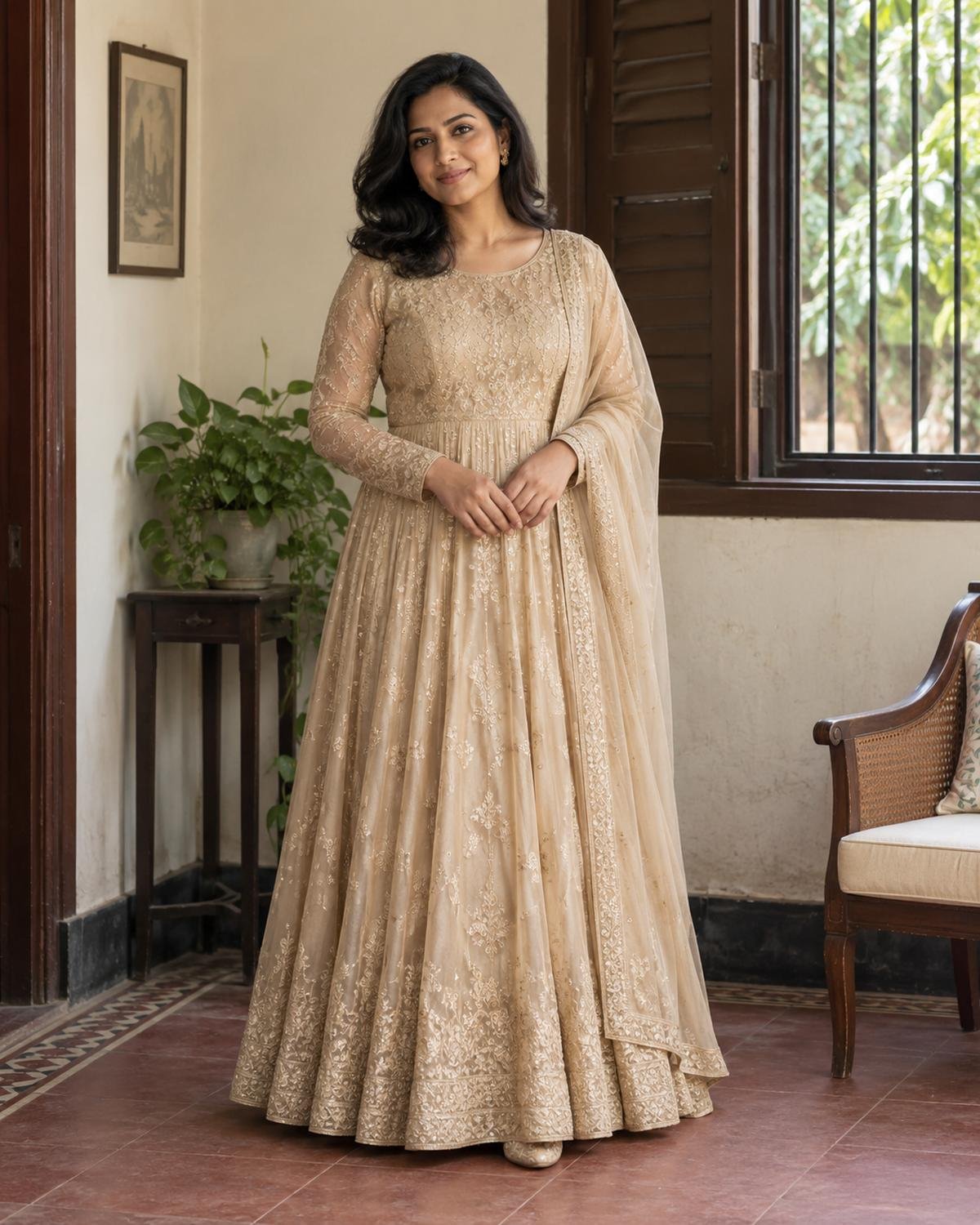 Woman in a champagne-gold Anarkali gown beside a wooden window in a contemporary Dhaka home.