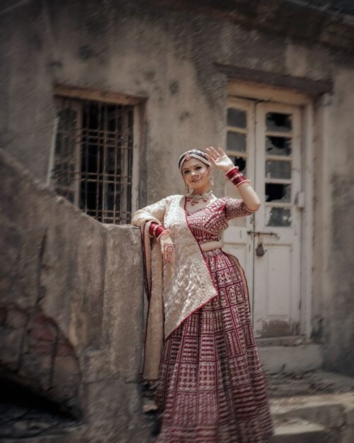 Model wearing a garnet red occasion outfit beside a heritage building