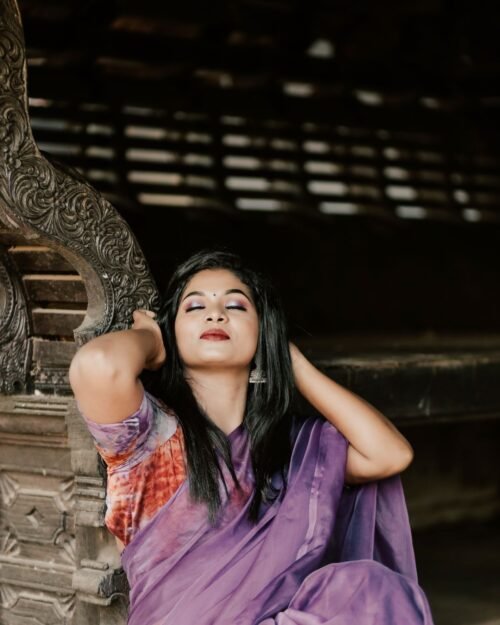 Model wearing a mauve saree seated on a wooden bench
